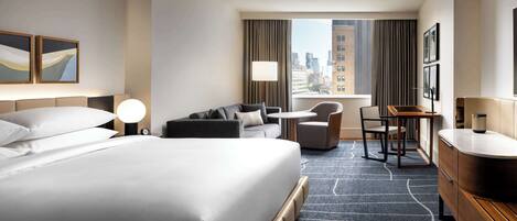 A hotel room with a large bed, a desk, a chair, and a view of the city.
