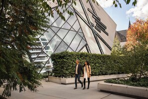 Un bâtiment moderne doté d’une façade en verre aux formes géométriques, avec une église en arrière-plan.