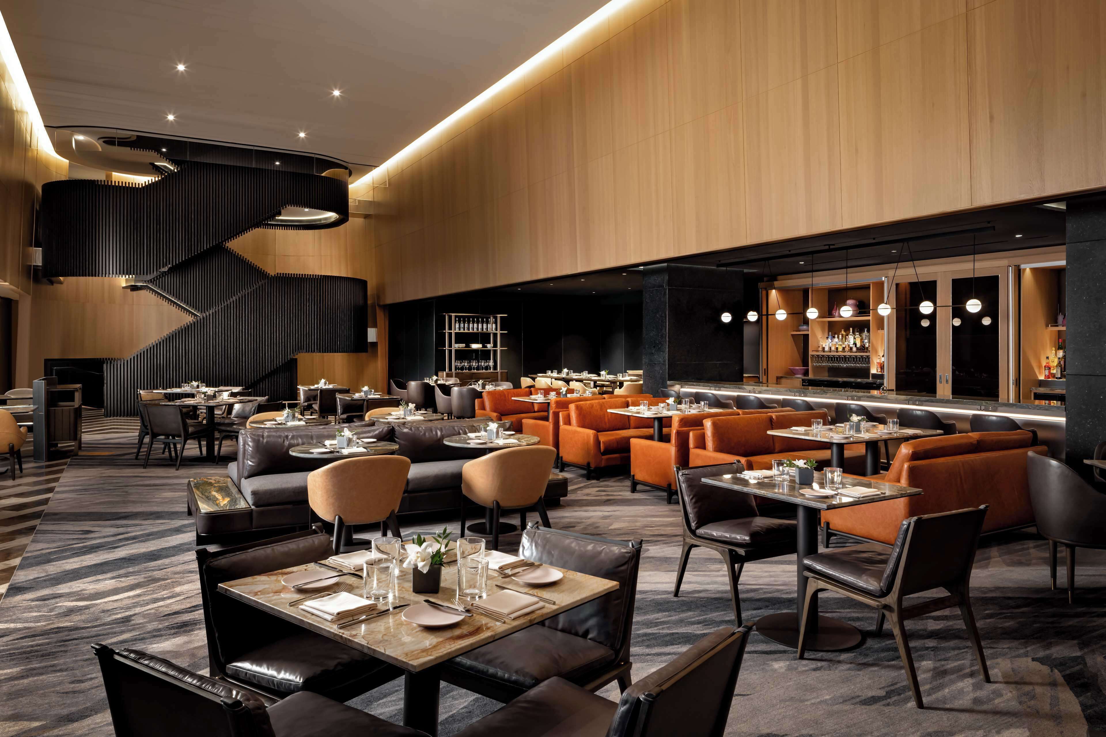 Een modern restaurant met een centrale trap, lederen zitplaatsen en een bar.