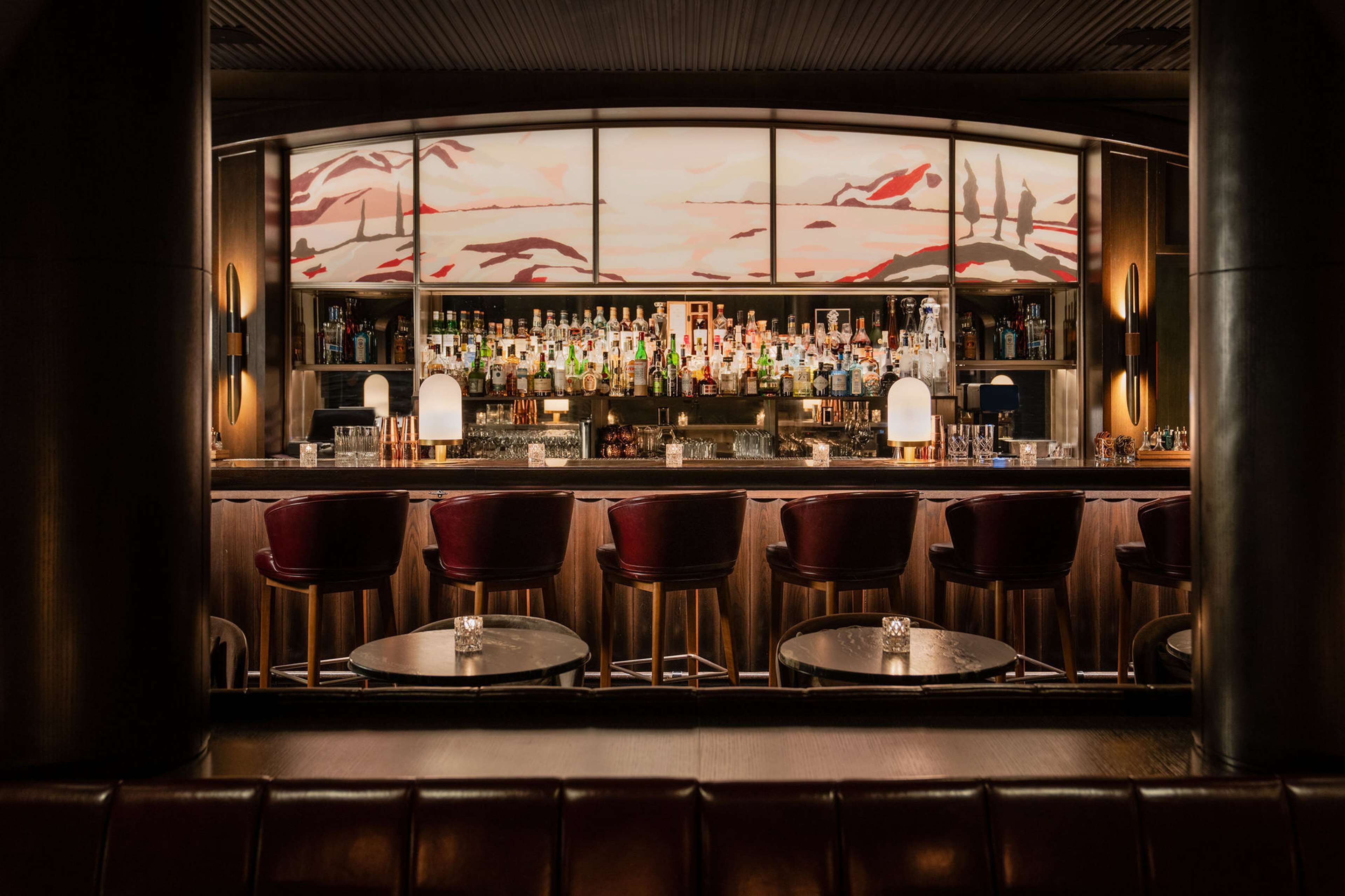 Een bar met een gebogen toonbank, diverse drankflessen en rode stoelen.