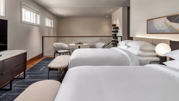 A modern hotel room with two beds, a desk, a chair, and a small table.