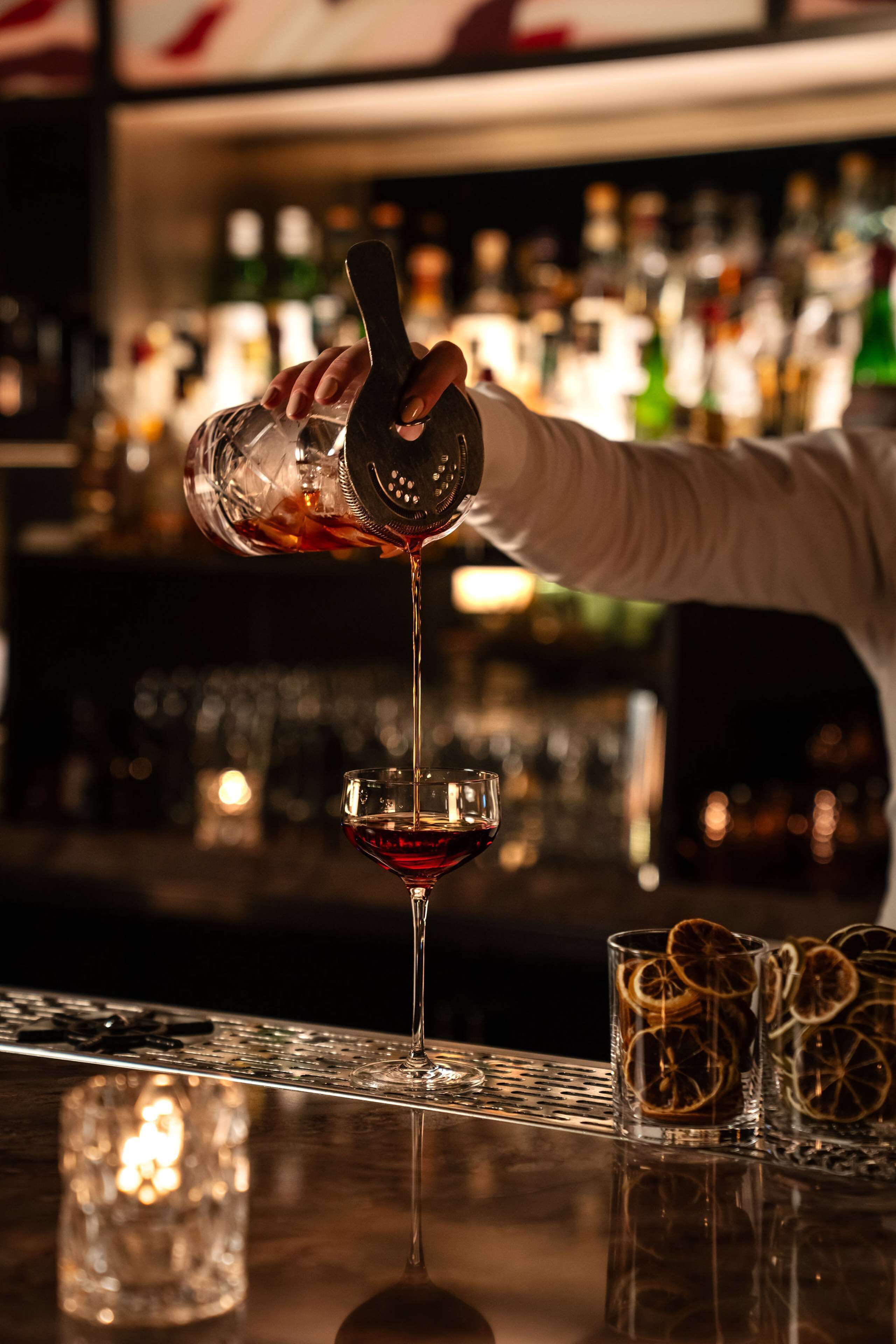 A bartender pouring a drink into a martini glass.