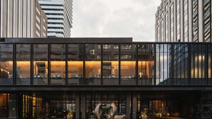 Un hotel moderno con fachada de vidrio, ventanas amplias y una entrada destacada con una escultura.