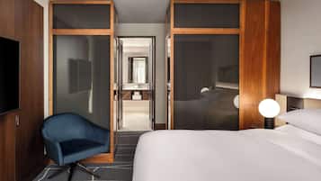 Een hotelkamer met een bed, een blauwe fauteuil, een televisie en een bureau met een lamp.