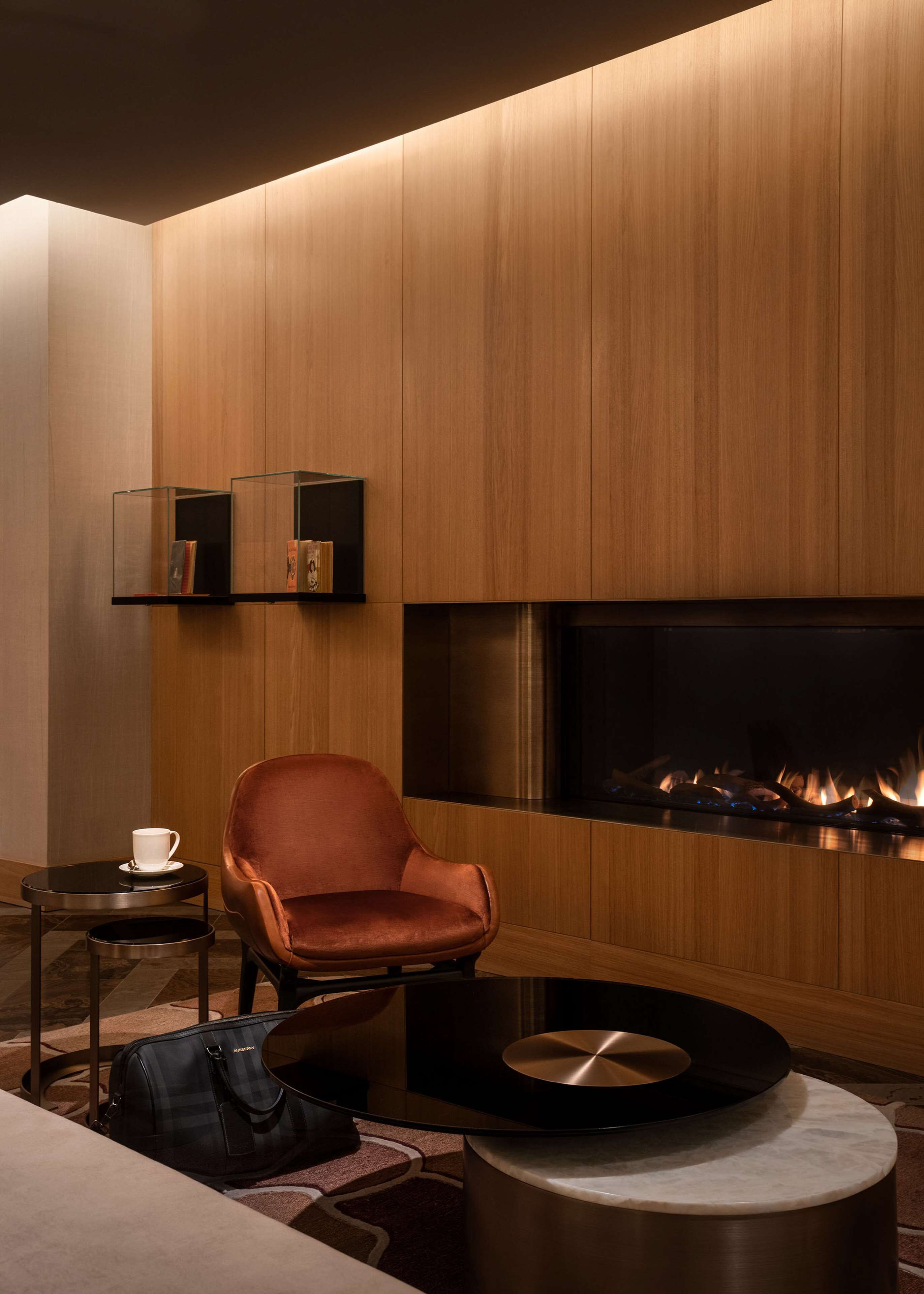 Een moderne woonkamer met een open haard, een leren fauteuil, een salontafel en een boekenplank.