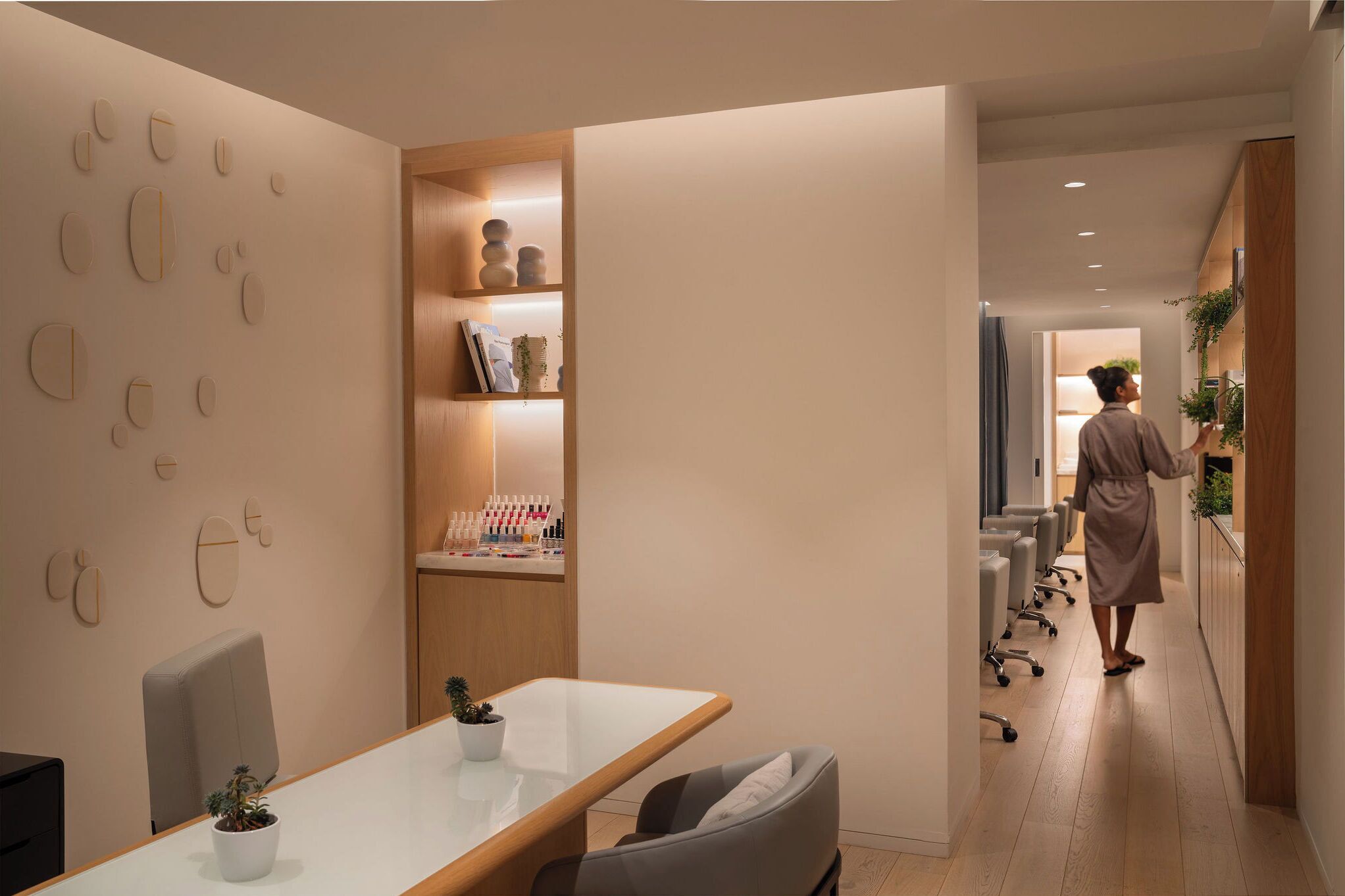 Un espace de bureau moderne avec une longue table, des chaises, une bibliothèque et une personne qui marche dans un couloir.