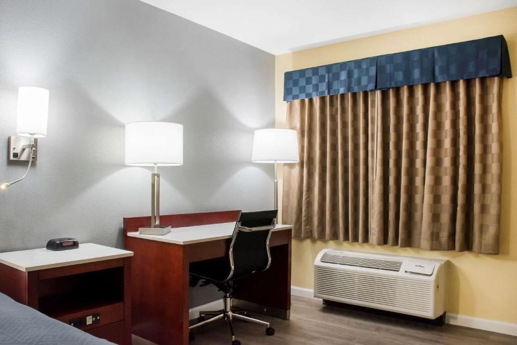 Une chambre d’hôtel équipée d’un bureau, de deux lampes, d’une chaise, d’un lit et d’un appareil de climatisation.