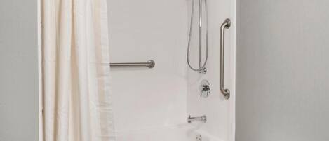 A bathroom with a shower, grab bars, and a white sink.