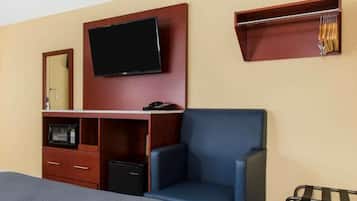 A hotel room with a bed, a TV mounted on the wall, a desk with a microwave, a chair, and a coat rack.