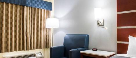 Habitación de hotel con cama, escritorio, silla, lámpara, luz empotrada en la pared y unidad de aire acondicionado.