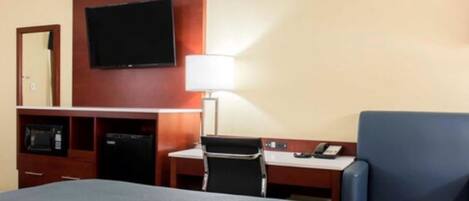 Habitación de hotel con cama, escritorio con lámpara, televisor montado en la pared y una silla azul.