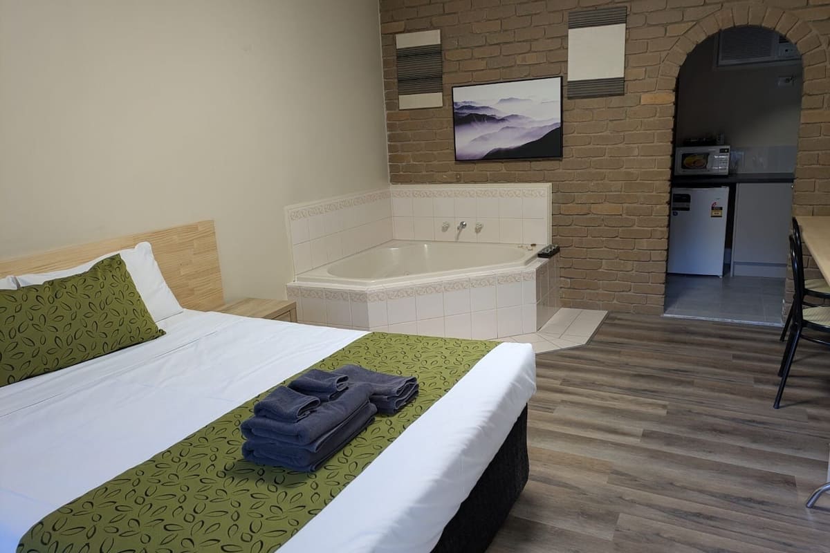 A hotel room with a bed, a large bathtub, a small kitchenette, and a picture on the wall.