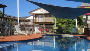 A swimming pool with lounge chairs and a building with a balcony in the background. - Albury Classic Motor Inn (Lavington)