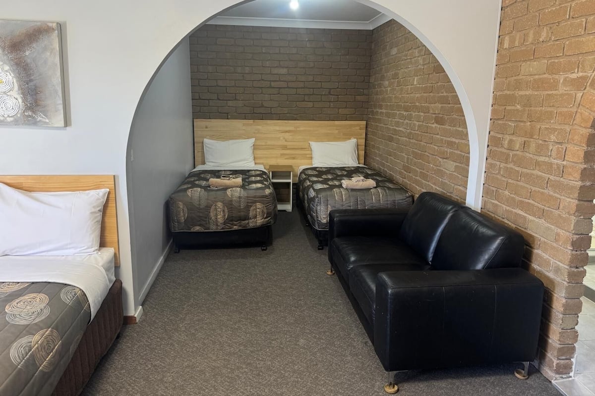 A small, cozy room with two single beds, a black leather sofa, and a brick wall.