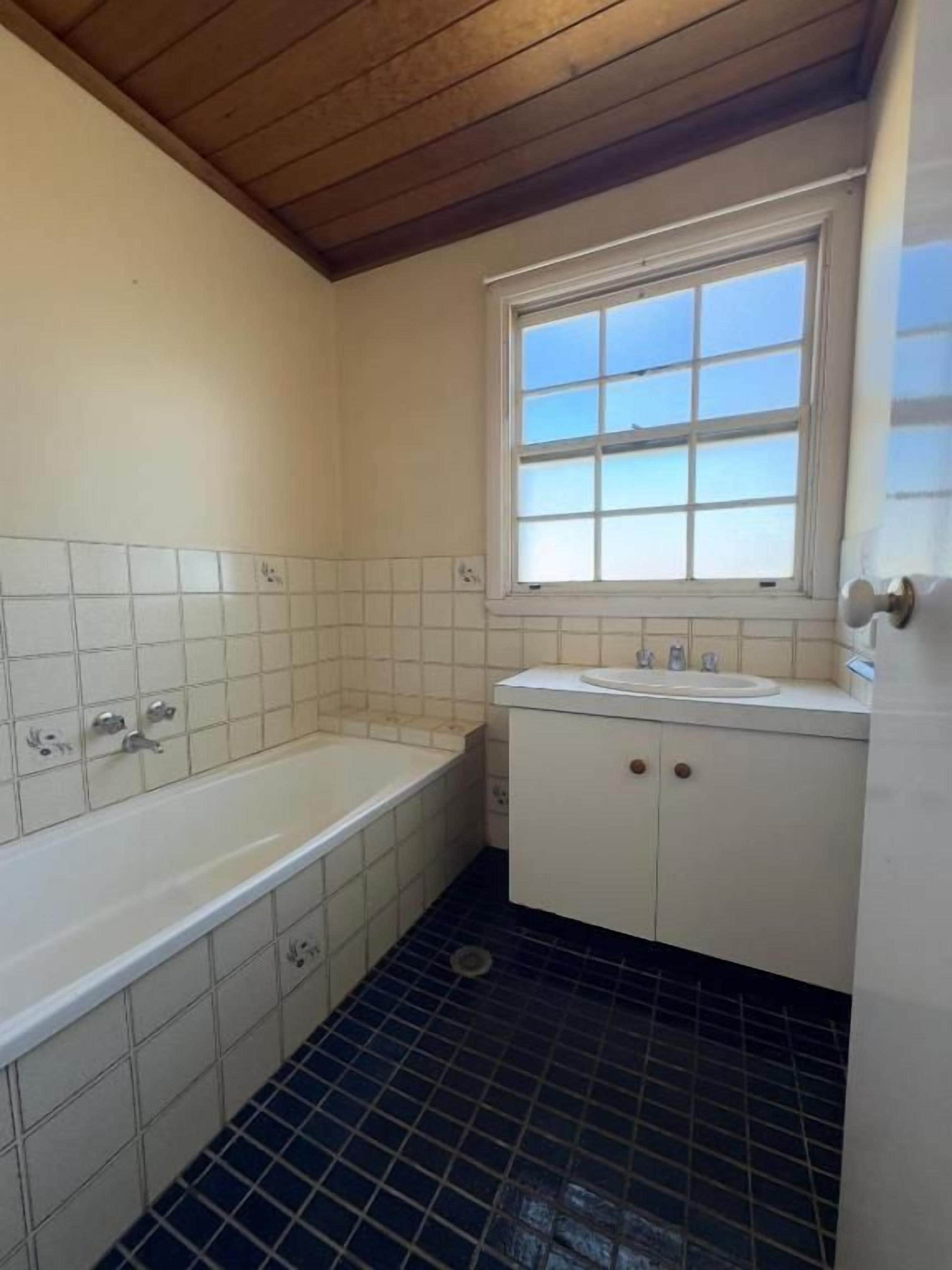 A bathroom with a bathtub, a window, and a sink.