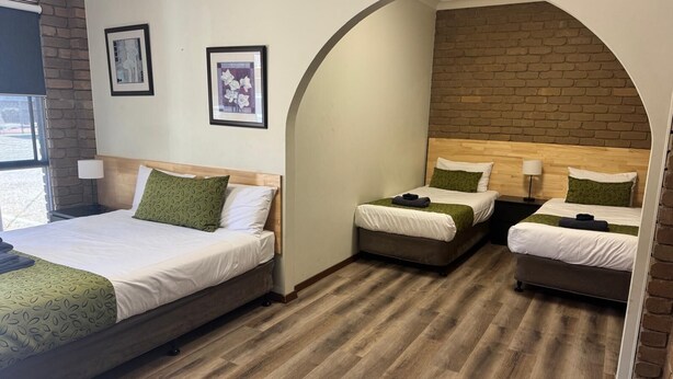 A hotel room with three beds, a brick wall, and two framed pictures on the wall. - Albury Classic Motor Inn (Lavington)