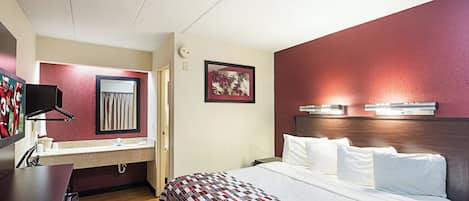 A hotel room with a bed, a desk with a computer, a mirror, and a picture on the wall.