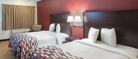 Quarto de hotel com duas camas, uma escrivaninha, uma cadeira e uma luminária.