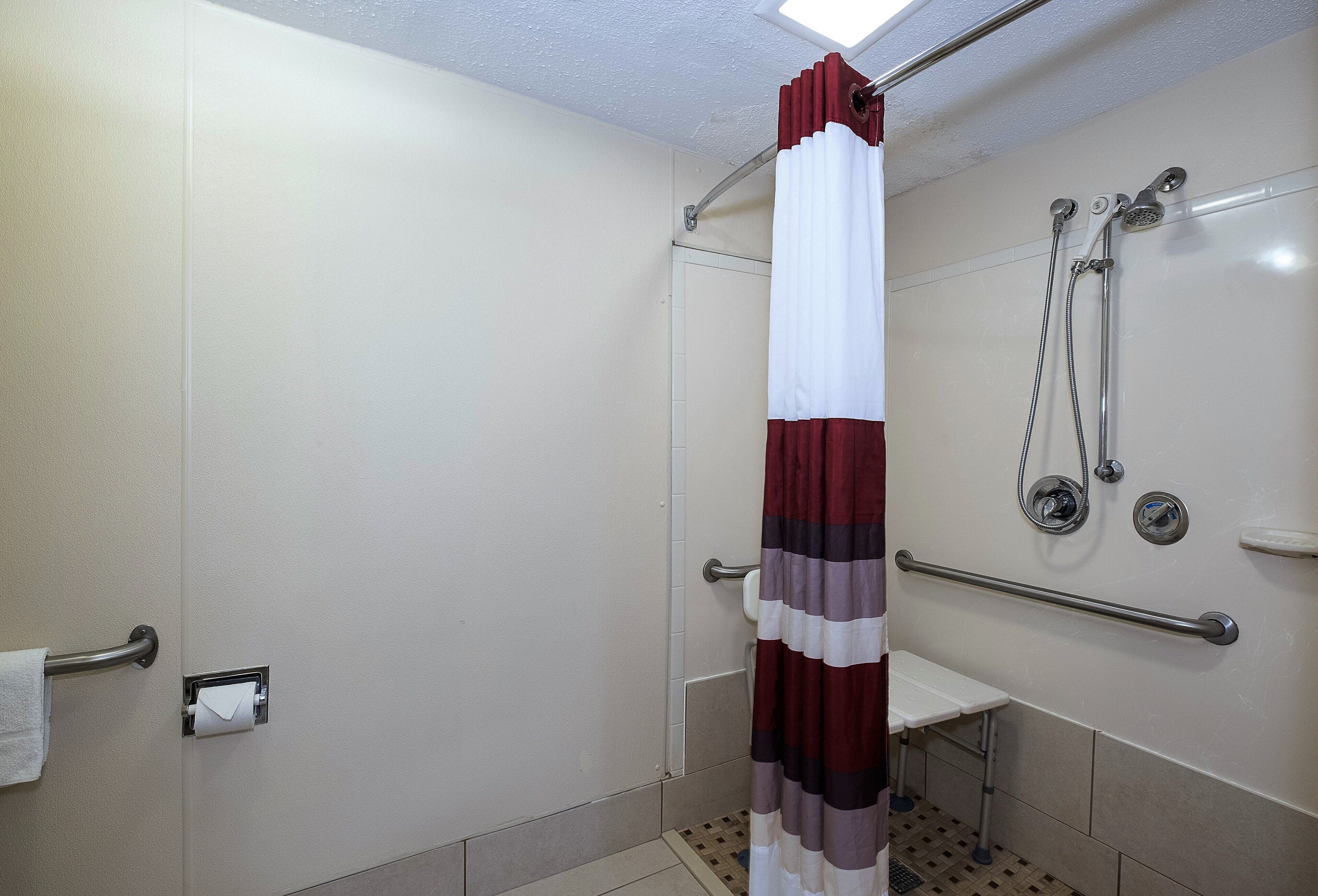 A shower with a white and maroon curtain, a handheld showerhead, and a grab bar.