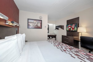 Habitación de hotel con cama, escritorio, televisor y espejo.