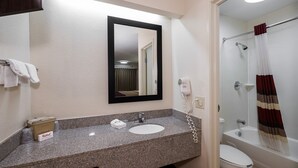 A bathroom with a granite countertop, a white sink, a mirror, a towel rack, a hairdryer, and a shower with a curtain. - Red Roof Inn Dayton - Fairborn/ Nutter Center (Fairborn)