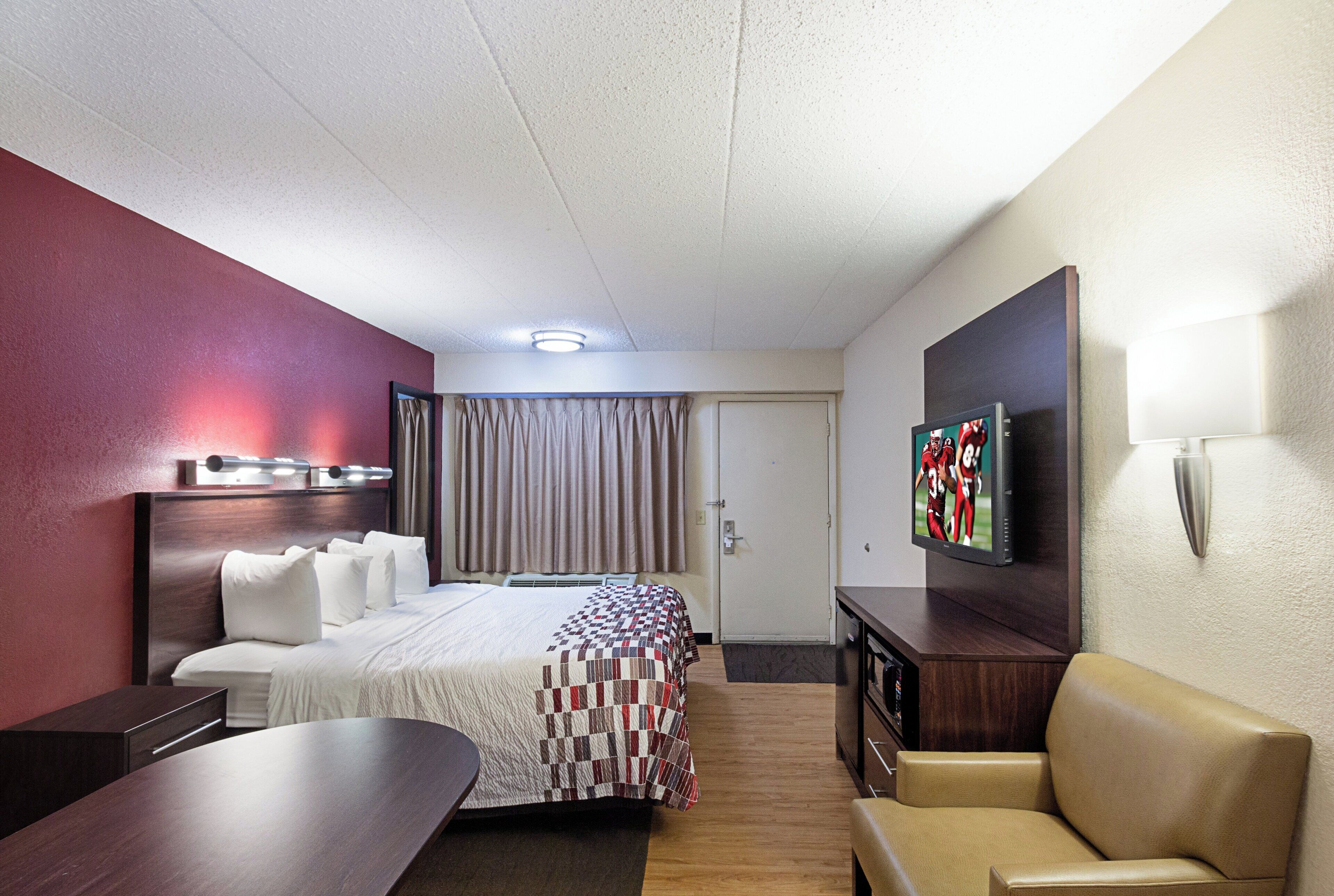 A hotel room with a bed, a desk, a chair, a television, and a door.