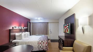 A hotel room with a bed, a desk, a chair, a television, and a door.