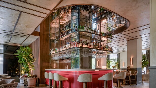Eine Bar mit einer gebogenen Glasscheibe, mehreren Flaschenregalen und Barhocker.