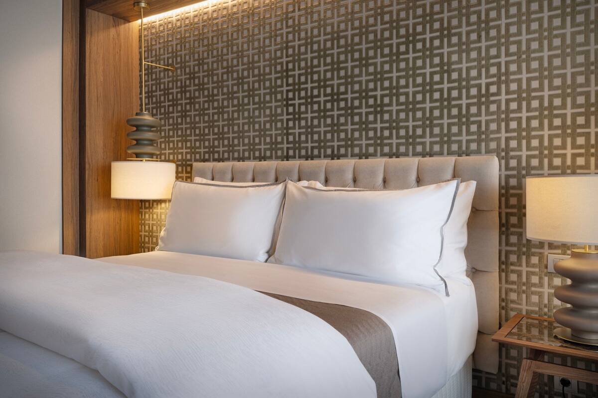 Un lit bien fait, avec une tête de lit, deux lampes de chevet et un mur décoré d’un motif.