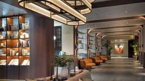 Eine moderne Lobby mit einer gebogenen Deckenleuchte, einer Sitzecke mit Sofa und Kissen sowie einem Bücherregal voller Bücher.