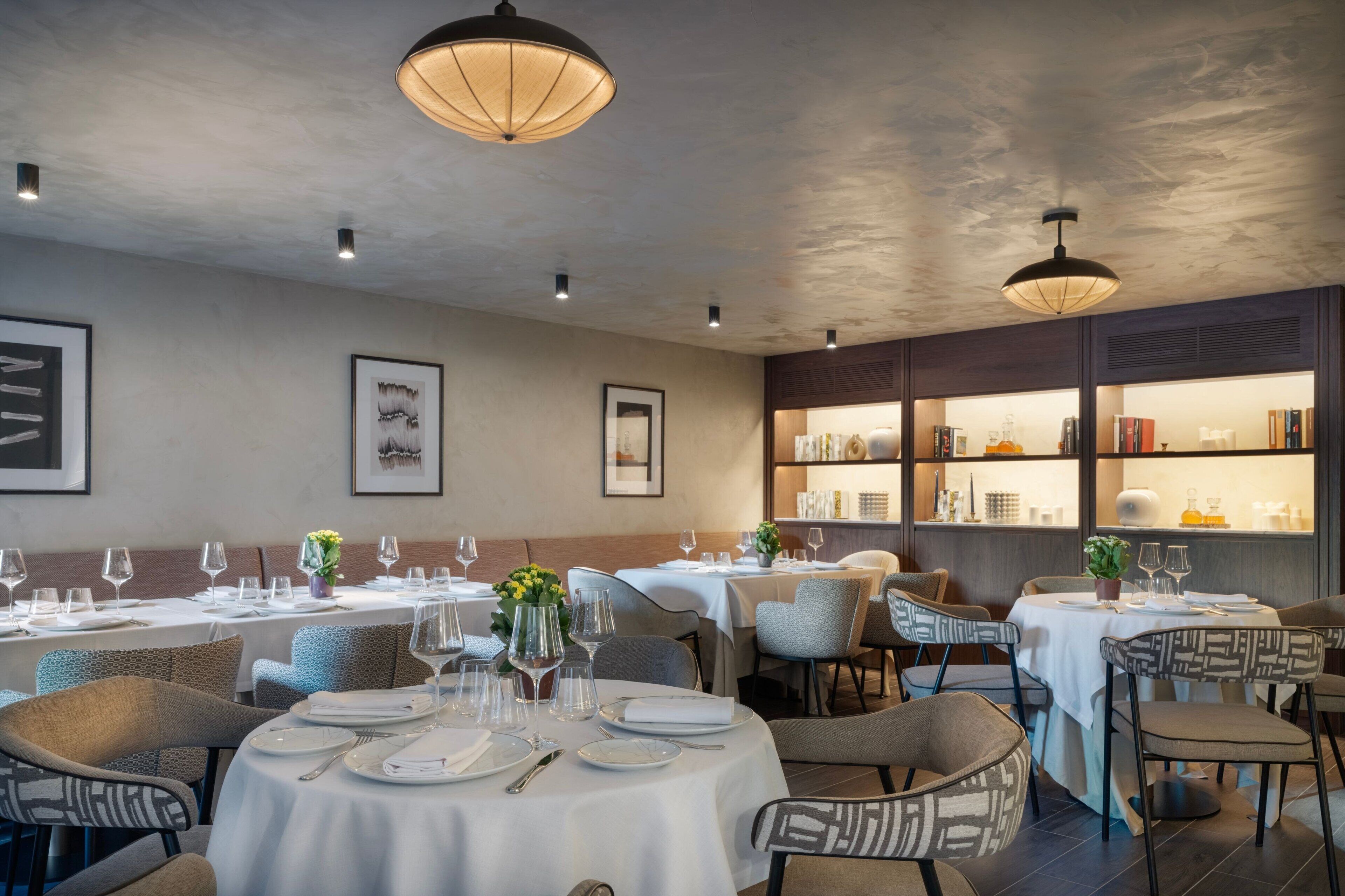 A restaurant with round tables set for dining, overhead lighting, and framed artwork on the walls.
