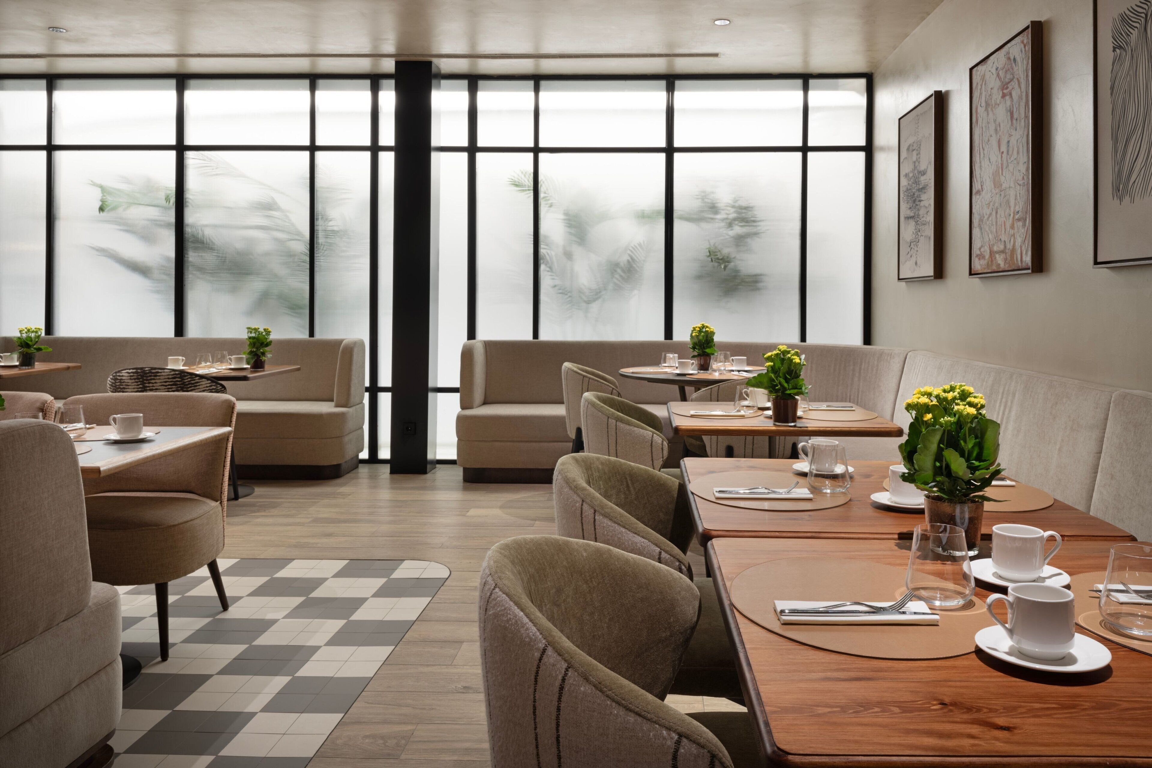 A modern dining area with tables and chairs, large windows, and artwork on the walls.