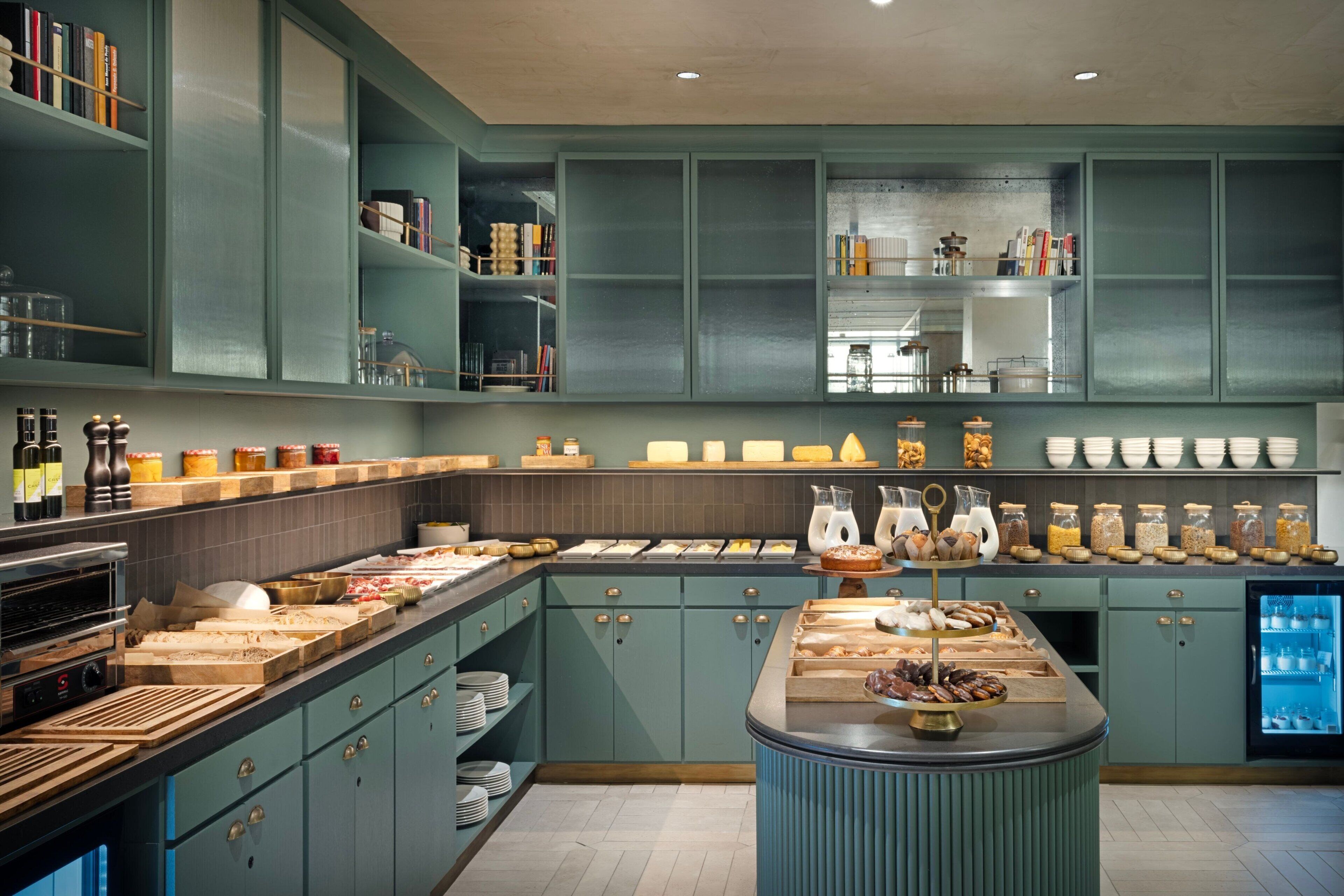 Una cocina moderna con armarios color turquesa, una isla central con exhibición de alimentos y un refrigerador con puertas de vidrio.