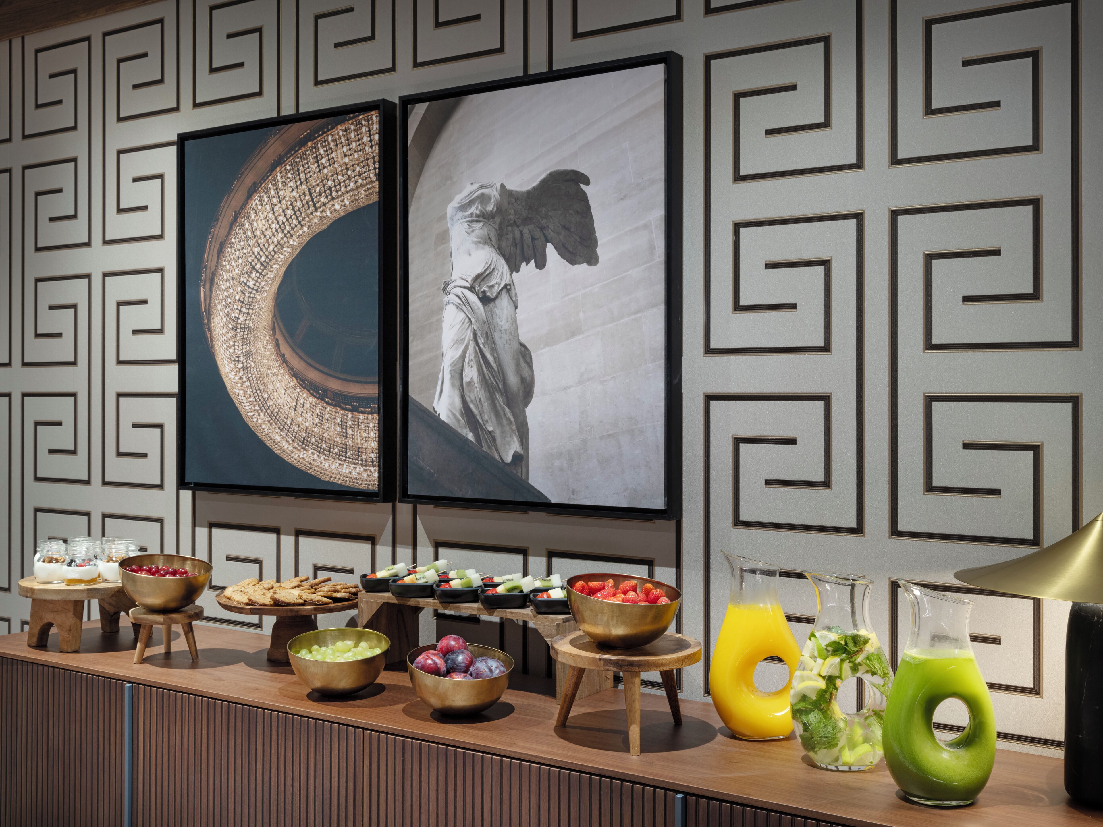 A buffet setup with various food items and drinks, framed artwork on the wall, and a modern interior design.