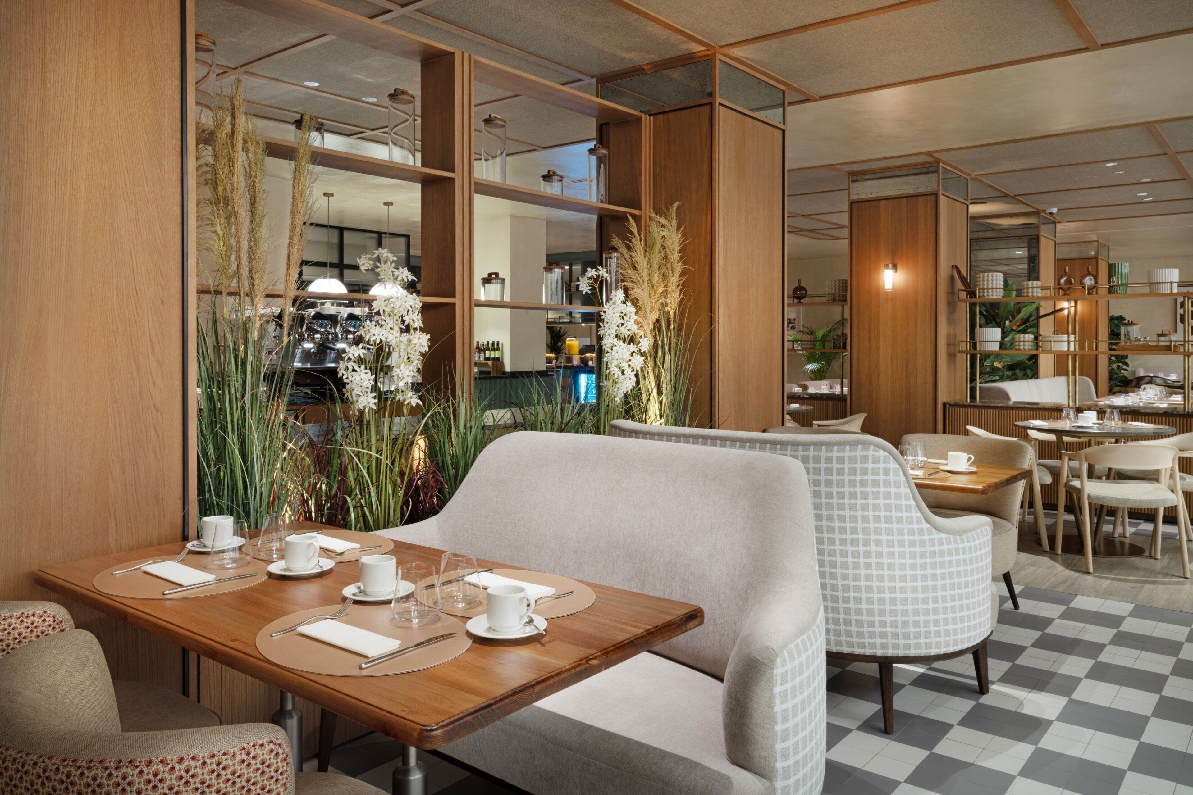 Un espace repas moderne avec des tables en bois et des sièges rembourrés, agrémenté d’un sol à carreaux et d’une décoration naturelle.