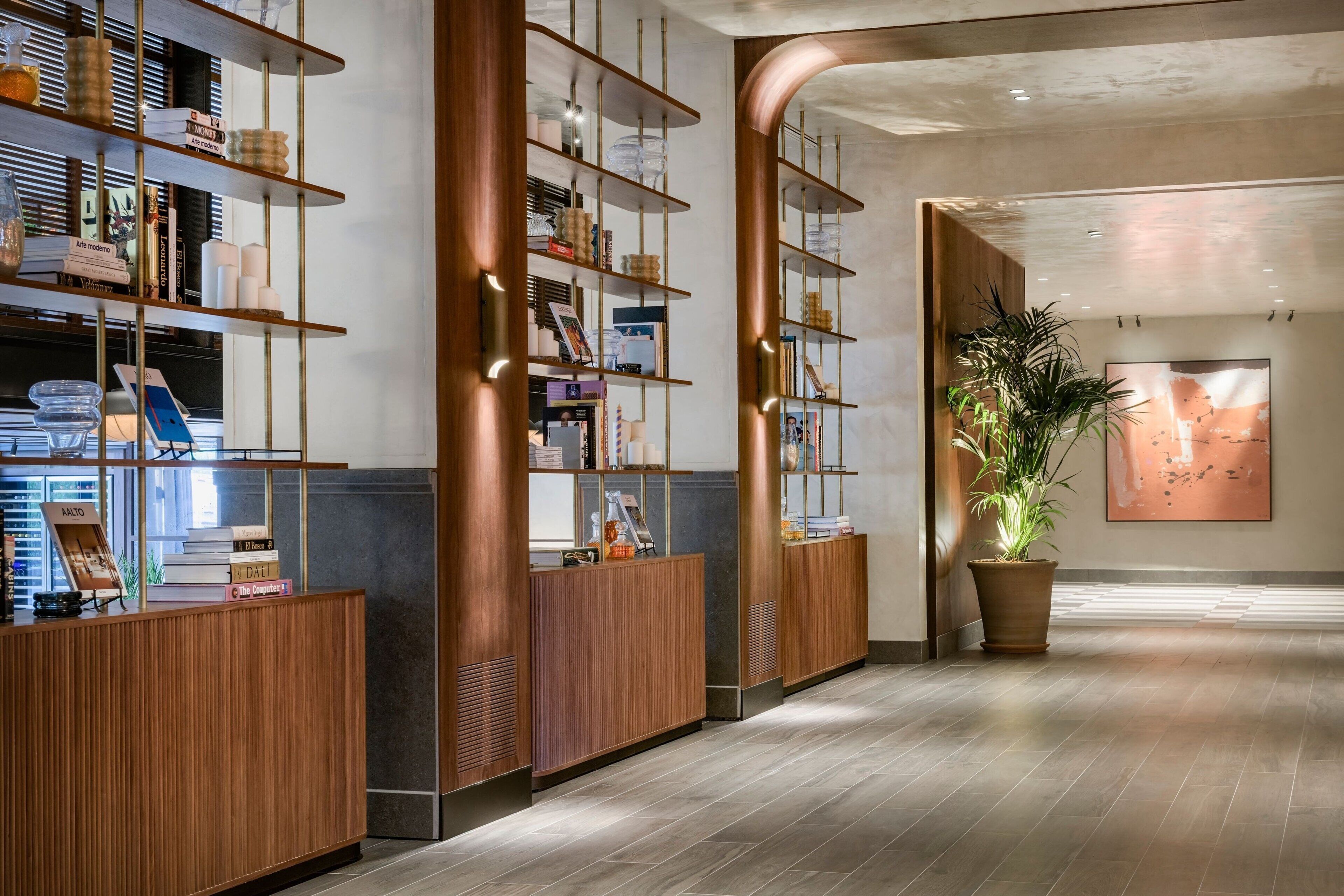 A modern reception area with wooden reception desks, metal shelving units, and a large potted plant.