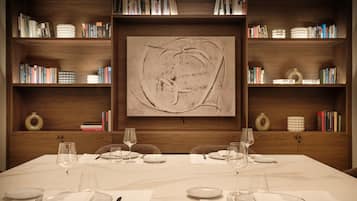 Mesa de comedor dispuesta para cuatro, con copas de vino y platos, flanqueada por estanterías llenas de libros y objetos decorativos.