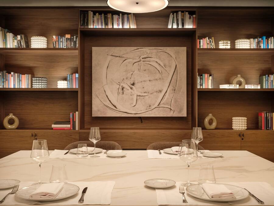 Mesa de comedor dispuesta para cuatro, con copas de vino y platos, flanqueada por estanterías llenas de libros y objetos decorativos.