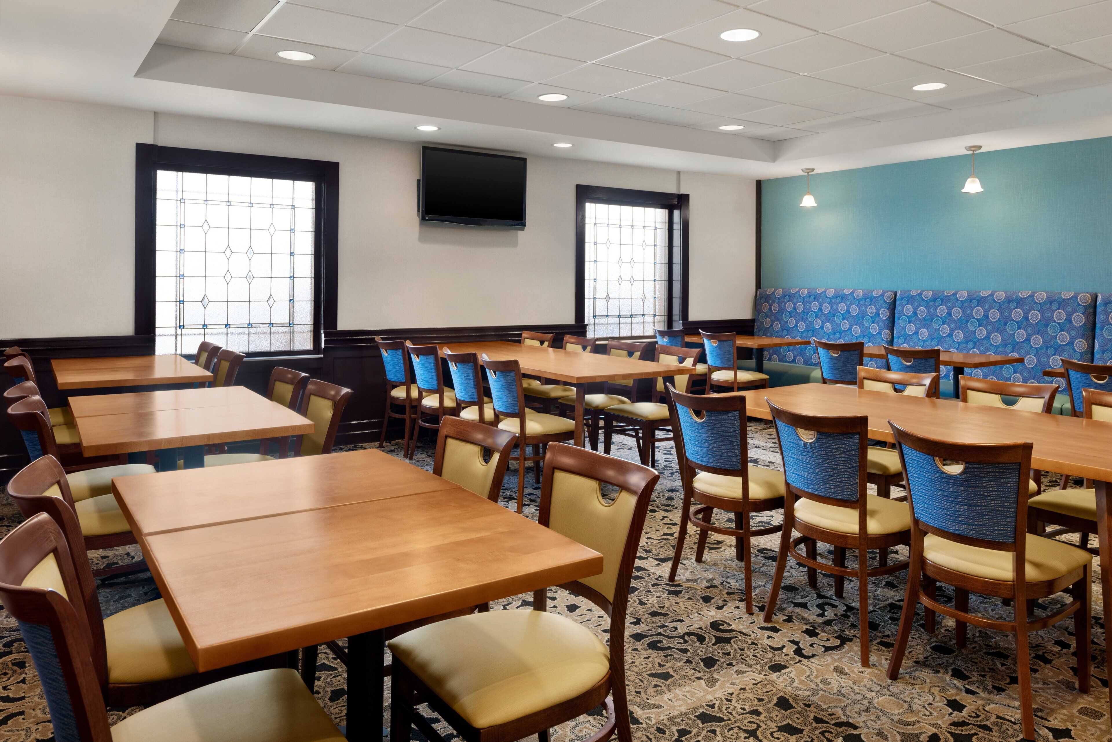 A conference room with multiple tables and chairs, a large screen, and patterned carpet.