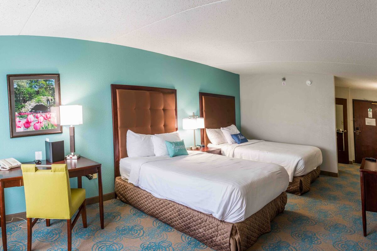 A hotel room with two beds, a desk with a chair, a telephone, and a framed picture on the wall.