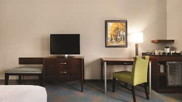 Une chambre d’hôtel équipée d’un lit, d’un bureau, d’une télévision, d’une chaise, d’une lampe et d’un réfrigérateur.