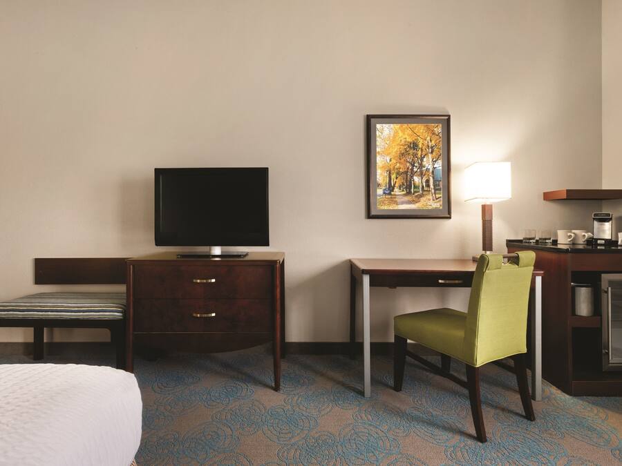 A hotel room with a bed, a desk, a television, a chair, a lamp, and a refrigerator.