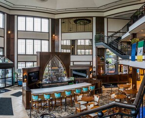 A spacious lobby with a central bar area, multiple seating arrangements, and a staircase leading to an upper level. - The Inn at Saint Mary's (South Bend)