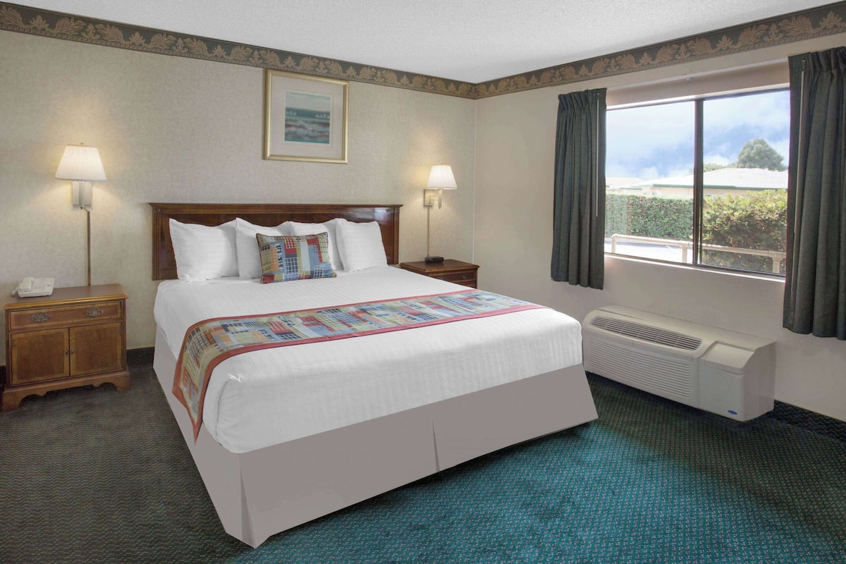 Quarto de hotel com uma cama grande, duas mesas de cabeceira com luminárias, uma janela com cortinas e ar-condicionado fixado na parede.