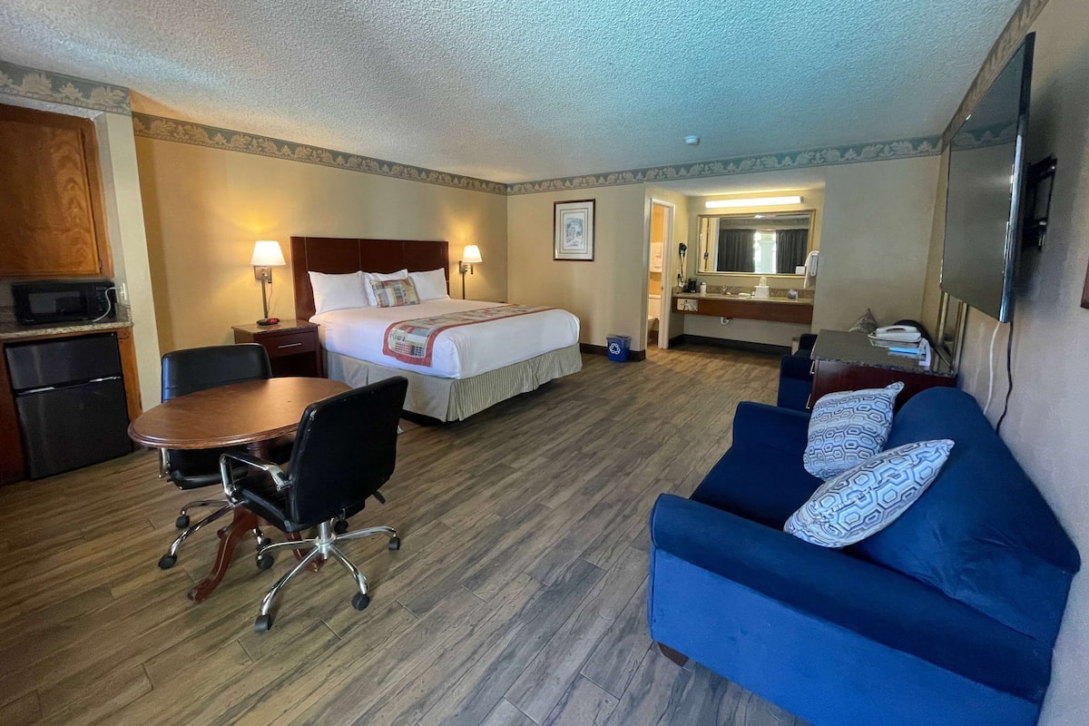 Quarto de hotel com cama, escrivaninha, sofá azul, micro-ondas, frigorífico e espelho de casa de banho.