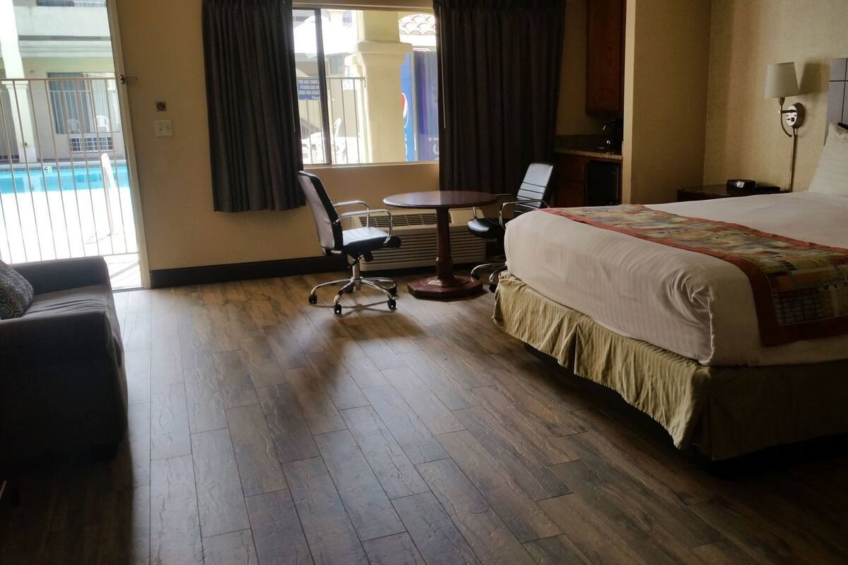 Quarto de hotel com cama, escrivaninha, cadeira e vista para a piscina.