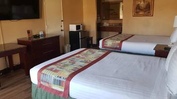 A hotel room with two beds, a desk, a television, a microwave, and a bathroom visible through an open door.