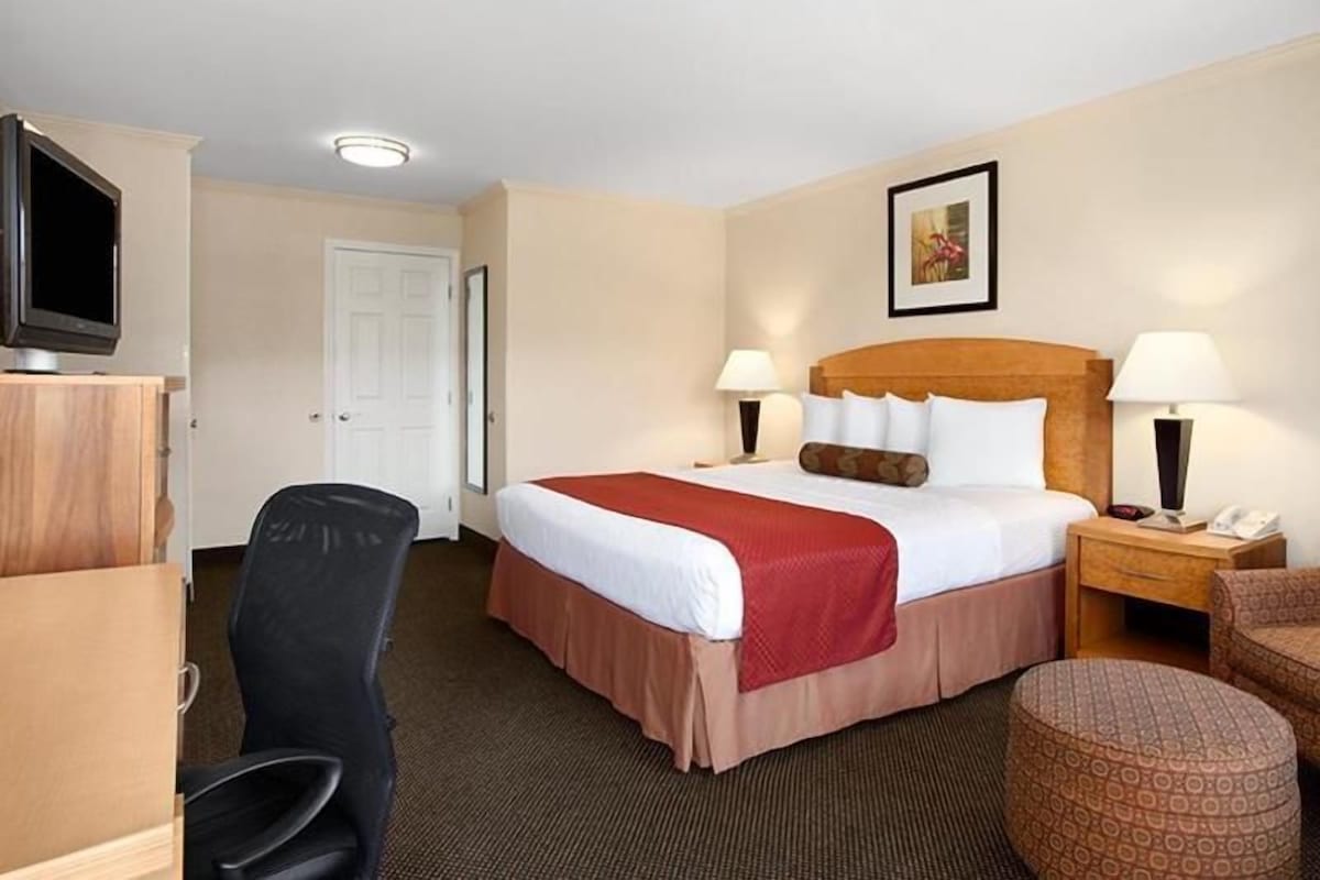 Ein Hotelzimmer mit Bett, Nachttischlampen, Schreibtisch, Stuhl, Fernseher und einer Tür.