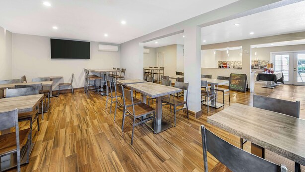 Un grand espace de salle à manger avec plusieurs tables et chaises, un téléviseur à écran plat fixé au mur et un coin cuisine à l’arrière-plan.