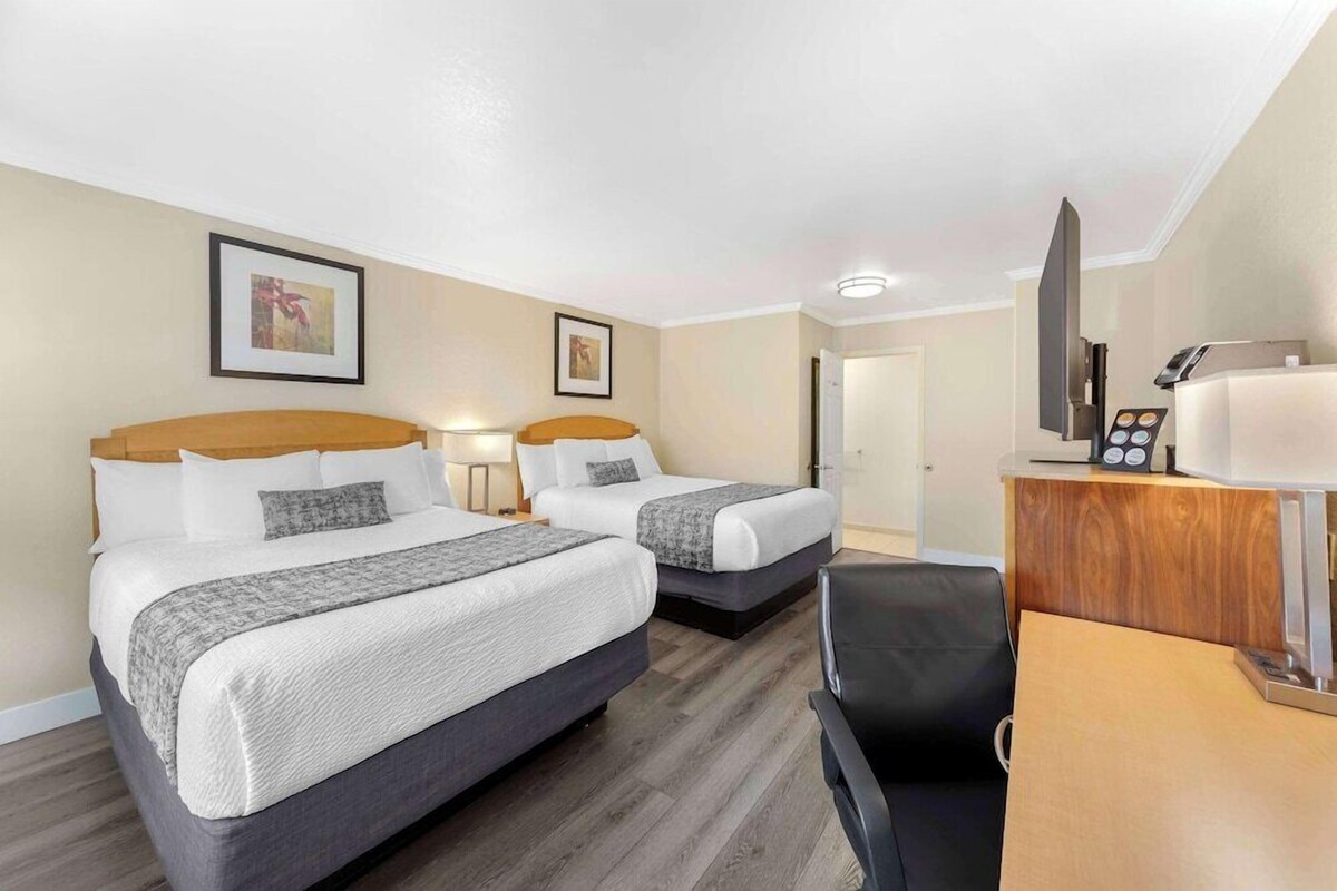 A hotel room with two beds, a desk, a chair, a TV, and a mirror.